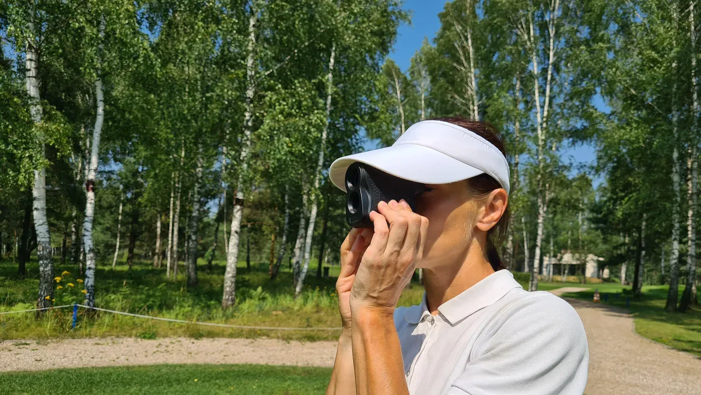 Golfare siktar med bästa golfkikaren bland björkar på banan