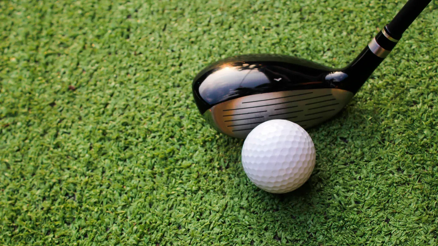 Klubbhuvud på bästa hybrid precis bakom golfboll på gräs