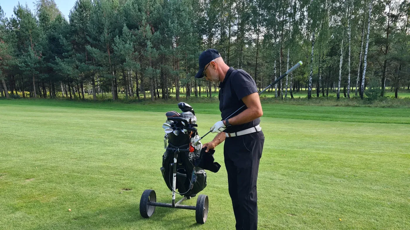 Golfare rengör klubba vid vagn på fairway bland träd