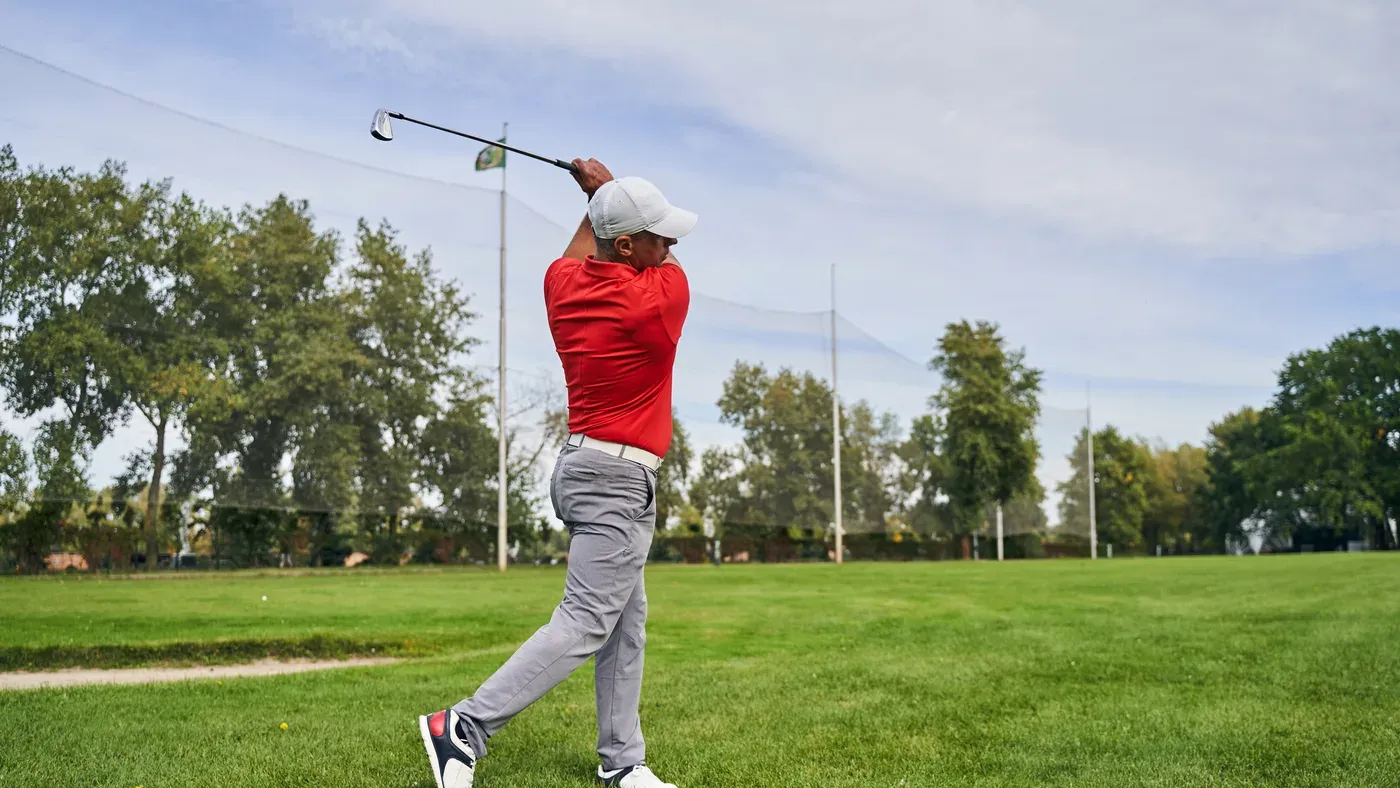Golfspelare i röd tröja fullföljer sving på inspelningsrange