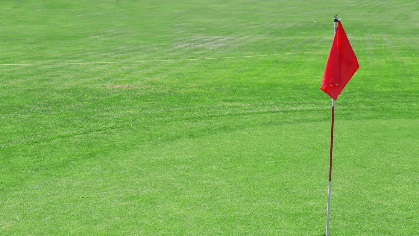 Rödmarkerad flagga står uppstucken på öppen golfgreen